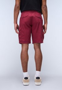 Pantaloni cargo bordeaux con molte tasche laterali e posteriori, realizzati in tessuto morbido, caratterizzati da un taglio dritto e orlo cucito.