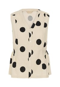 Blouse beige sans manches avec grands pois noirs et col en V.