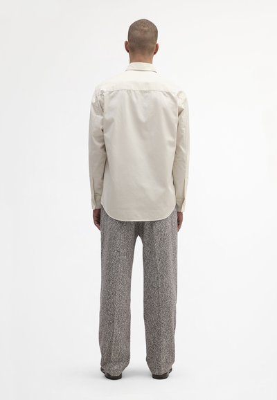 Beige langærmet skjorte med en blød tekstur, knap-ned krave, buet kant, båret med grå teksturerede vide bukser.