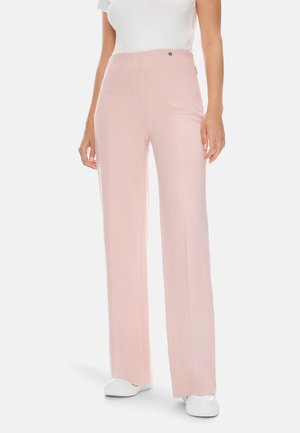Helles pinke, weite Hosen aus glattem Stoff, mit hoher Taille und dezenten Vordernahtdetails, kombiniert mit weißen Sneakern.