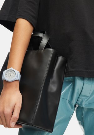 Sort læder tote bag med en glat tekstur og struktureret design, holdt i en hånd iført et lyseblåt tekstureret ur.