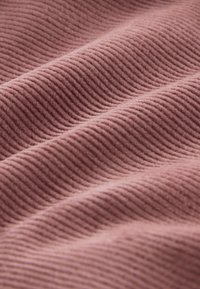 Tissu côtelé rose doux avec des lignes parallèles en relief créant un motif de surface texturé et ondulé.