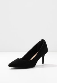 Chaussure à talon haut en daim noir avec un bout pointu et un talon fin. Comprend un chaussant bas et une texture lisse.