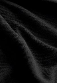 Tissu tricoté noir avec une texture douce, présentant des stries horizontales subtiles et des plis délicats, réfléchissant la lumière dans des nuances variées.