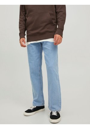 Jeans de mezclilla azul claro con un corte relajado, usados con una sudadera con capucha marrón y zapatillas negras con suelas y cordones blancos.