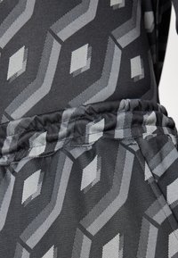 Grå mønstret stof med geometriske former, herunder zigzag-mønstre og diamanter, med en blød tekstur og detaljeret, samlet talje.