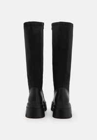Black knee-high boots featuring a sleek fabric upper, leather accents, a chunky sole, and a zipper closure on the side.