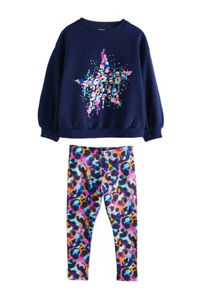 Tamnoplava majica dugih rukava s grafikom šarenog zvijezde, uparena s vibrantnim, uzorkovanim tajicama koje imaju višebojni apstraktni print.