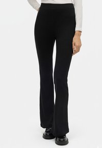 Pantalones acampanados negros con textura de canalé y una cinturilla alta, que presentan una superficie suave y una silueta ajustada, combinados con zapatos negros gruesos.