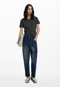 Camiseta gris con logo en relieve, pantalones cargo azules con múltiples bolsillos y zapatillas con un diseño estampado, complementadas por un bolso cruzado ligero.