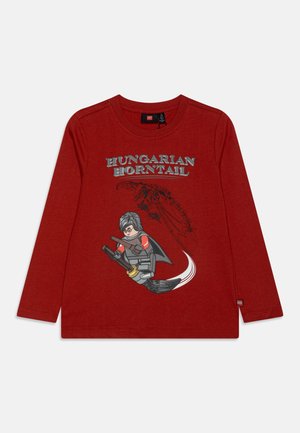 Czerwona koszula z długim rękawem z napisem "Hungarian Horntail" oraz postacią czarodzieja w stylu LEGO lecącą na miotle, z sylwetką smoka w tle.