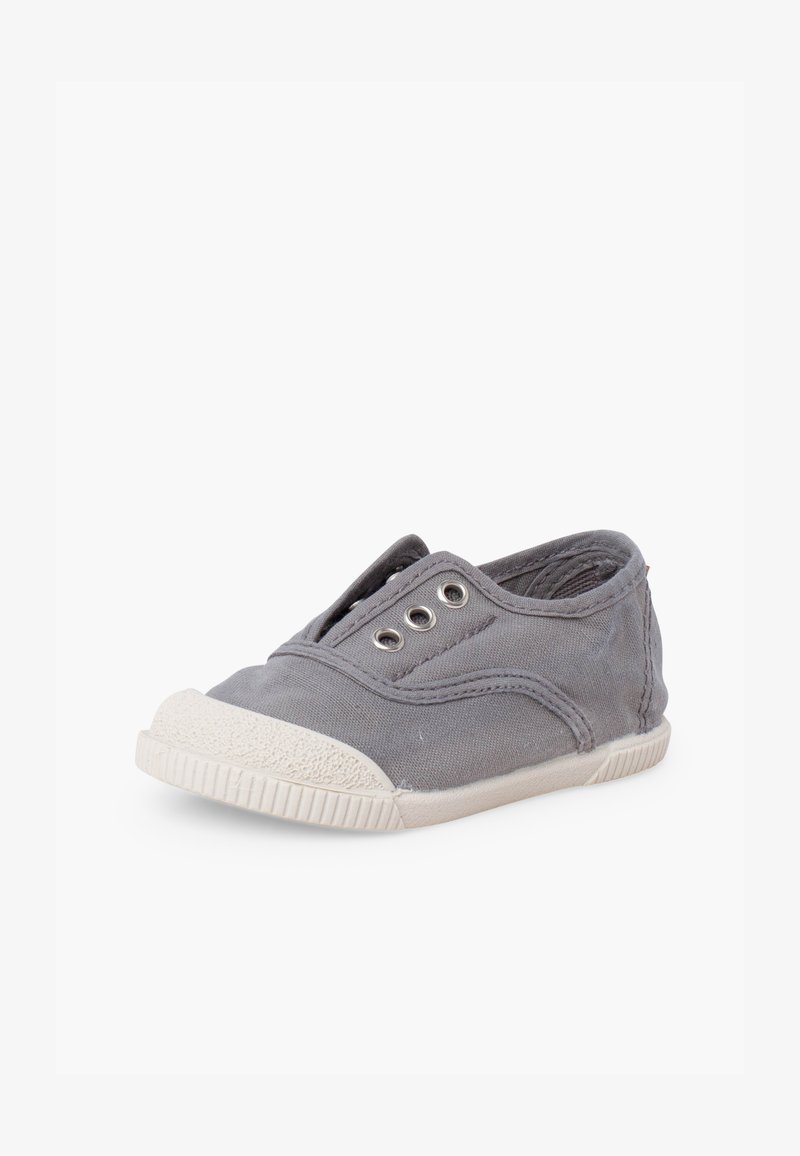 Baskets slip-on en toile grise avec semelle et embout en caoutchouc blanc, présentant trois œillets métalliques pour les lacets, sans lacets.