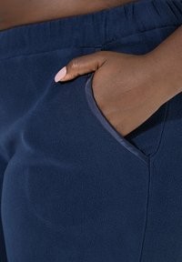 Marineblauwe fleece joggers met een zachte textuur, elastische tailleband en zijzakken. Geaccentueerd met gladde stof rond de zakranden.