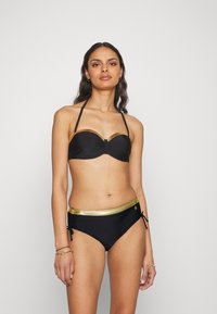 Biquíni preto com um top sem alças, adornado com uma faixa dourada e um detalhe de nó à frente, acompanhado de calções de brim de cintura alta com elementos dourados e laços.