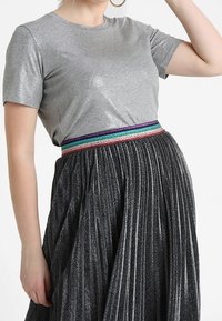 Gray short-sleeve top with a smooth texture, paired with a pleated black skirt featuring a multicolored glittery waistband.