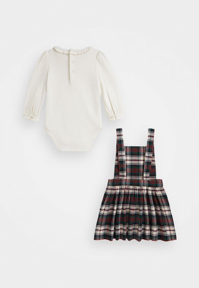 Body de mangas longas branco com colarinho franzido e fecho de botão, combinado com um vestido em xadrez verde e vermelho com alças ajustáveis e saia rodada.