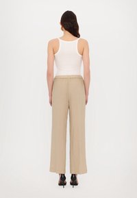 Débardeur blanc à fines bretelles associé à un pantalon ample beige clair, avec une taille élastique et une finition en tissu texturé.