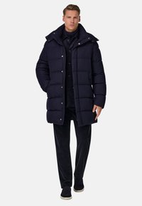 Navy modrý péřový kabát s vysokým límečkem, předními knoflíky a dvěma postranními kapsami, v kombinaci s černými kalhotami a botami. Hladký povrch, izolační design.