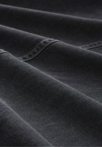 Nahaufnahme von gefaltetem schwarzem Denimstoff, der die Textur und sichtbare Nahtsteppungen zeigt.