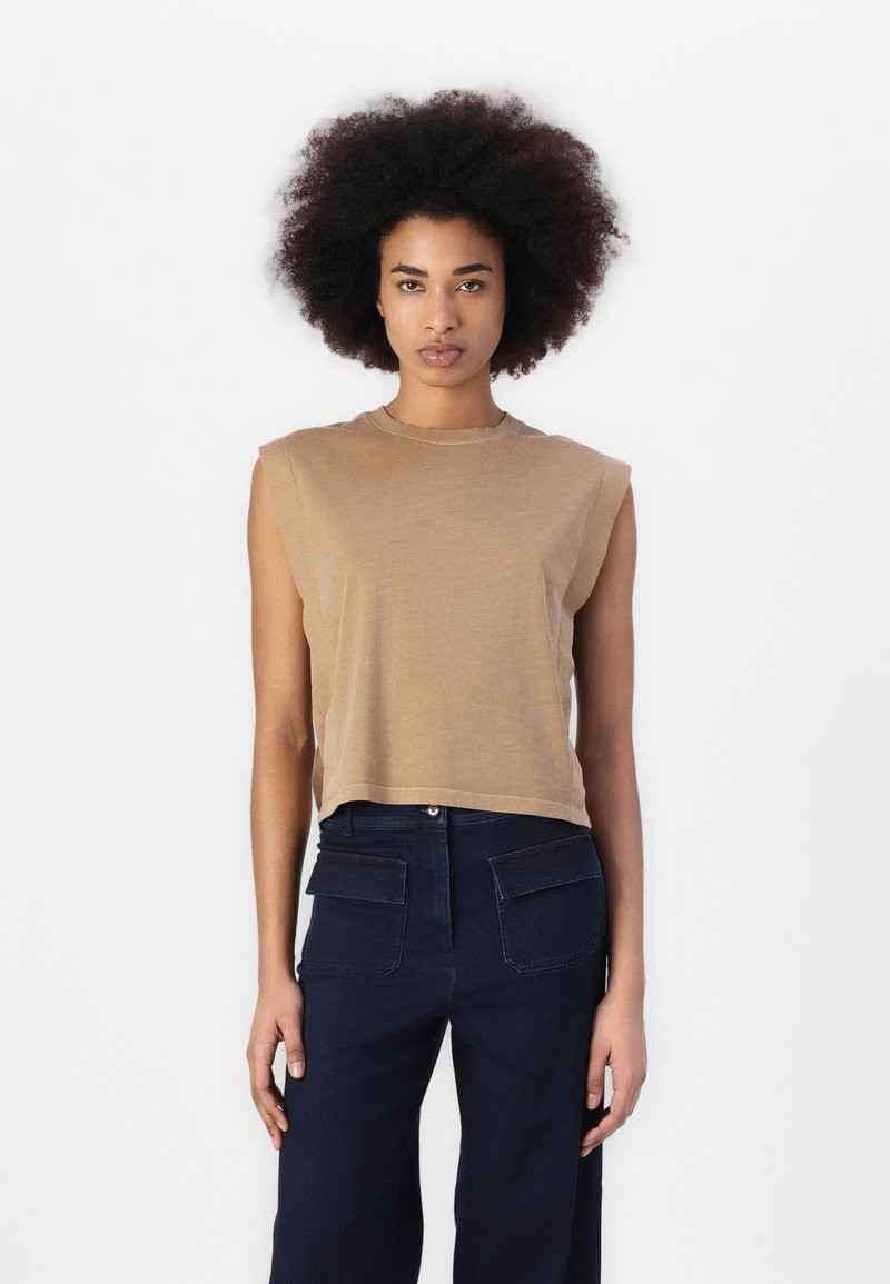 Top marrón sin mangas con cuello redondo, hecho de una tela suave, y combinado con pantalones de pierna ancha en azul oscuro que tienen bolsillos traseros.