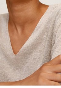 Light gray V-neck sweater made of a textured, sparkly knit material, featuring short sleeves and a relaxed fit. Skin-toned arms visible.