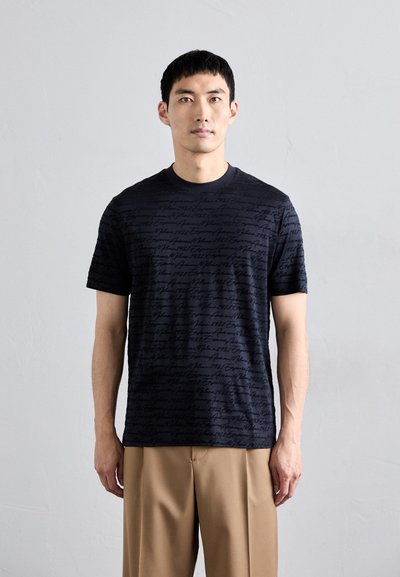 Schwarzes T-Shirt mit einem sich wiederholenden Schriftmuster, kurzen Ärmeln und rundem Ausschnitt. Hergestellt aus weichem Stoff mit einer strukturierten Optik.