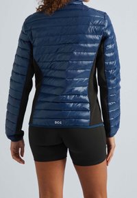 Laivastonsininen toppatakki, jossa on vaakasuorat tikatut osiot, mustat sivut ja korkea kaulus. Takareunassa pieni logo.