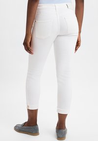 Witte denim skinny jeans hebben een opgerolde zoom, subtiele achterzakken en een gladde textuur. Gecombineerd met grijze loafers voor contrast.