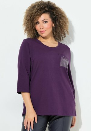 T-shirt viola a maniche lunghe con colletto rotondo e taschino sul petto caratterizzato da un design con borchie argentate. Tessuto morbido con vestibilità comoda.