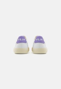 Hvite kanvas sneakers med lyse lilla hælaksenter og hvit logo. Har en beige gummisal. Rent design, minimal detailing.