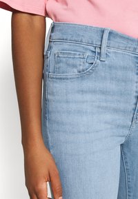 Ljust blå denimjeans har hög midja, framfickor och subtila sömmar. Tyget har en mjuk textur med en lätt blekning.