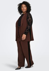 Brown two-piece outfit with a sleeveless vest and matching pants. Textured black long-sleeve top underneath. Pants have black side stripes.