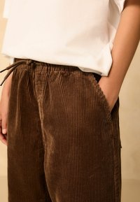 Braun Cordhosen mit vertikaler Rippung, ausgestattet mit einem elastischen Bund und Kordelzug. Taschen auf beiden Seiten. Weicher Stoff.