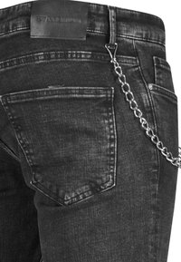 Los jeans de mezclilla negra presentan una etiqueta de cuero, un detalle de cadena y dos bolsillos traseros con acentos de costura. La tela tiene una textura sutil.
