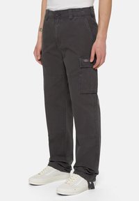 Mörkgrå cargo-byxor gjorda av slitstarkt tyg, med sidofickor, en avslappnad passform och sömnadsdetaljer. I kombination med vita sneakers.