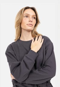 Felpa grigia carbone con maniche lunghe, polsini a costine e scollo rotondo. Tessuto morbido con vestibilità comoda, caratterizzata da dettagli di design minimi.