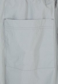 Jasnoszara tkanina z płaską kieszenią i widocznym przeszyciem. Faktura jest lekko pofałdowana, co odzwierciedla swobodny styl.