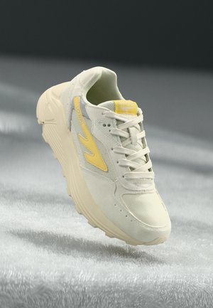 Sneaker beige clair avec des accents jaunes et une tige en mesh texturé. Présente une semelle rembourrée et un design à lacets. Silhouette basse.