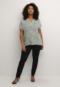 Blusa verde e nera con stampa leopardata a maniche corte realizzata in tessuto leggero, design a scollo a V, abbinata a pantaloni neri aderenti e sandali con tacco.