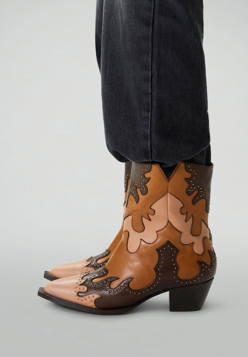 Bottes de cow-boy brunes et beiges avec un bout pointu, en cuir texturé, et des accents de broderie décorative. Talon bloc bas, motifs de flammes complexes.