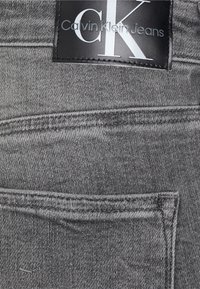 Vaqueros de denim gris con un acabado texturizado, que cuentan con un parche de cuero negro de Calvin Klein Jeans en la cintura y detalles de costura en contraste.
