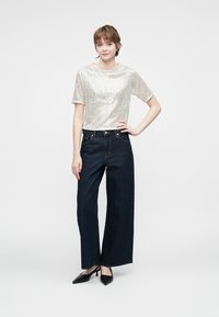 Top plateado con lentejuelas y mangas cortas combinado con pantalones de mezclilla oscuros de tiro alto y anchos, y tacones negros de punta.