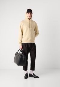 Felpa con cappuccio beige, pantaloni neri, borsa di pelle nera, mocassini neri e calzini bianchi. Design semplice, texture morbida, vestibilità casual.