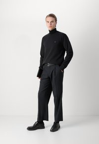 Black turtleneck sweatshirt features a small logo, paired with tailored black trousers and black lace-up shoes, held with a slim black belt.