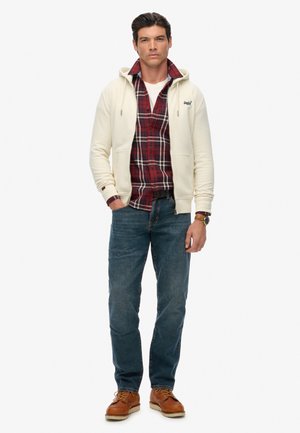 White zip-up hoodie over a red and black plaid shirt, blue jeans, and brown lace-up shoes. Casual outfit with a layered design.