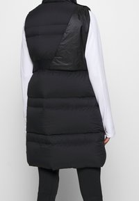 Sort puffer-vest med varieret tekstur, der har en blank skuldersektion og en længere, quiltet ryg. Den er uden hætte og har sidesømme.