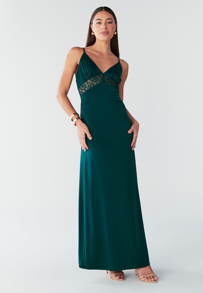 Abito maxi verde smeraldo con scollo a V, dettagli in pizzo sul corpetto e spalline sottili, realizzato in tessuto liscio e fluido.