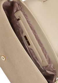 Beige taske indvendig med en tekstureret cremefoering, der har en lynlåslomme og en guldfarvet hardwareaccent med logo-detalje.