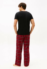 Camiseta negra de manga corta y pantalones de pijama a cuadros rojos con líneas blancas y negras, textura suave, corte relajado y sin logotipos visibles.