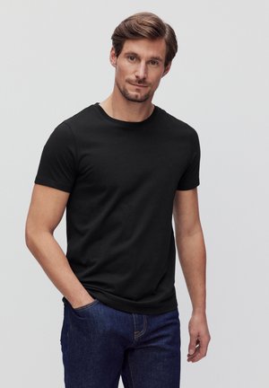 T-shirt en coton noir avec un col rond et des manches courtes, design ajusté. Associé à un jean en denim bleu. Texture lisse, style simple.